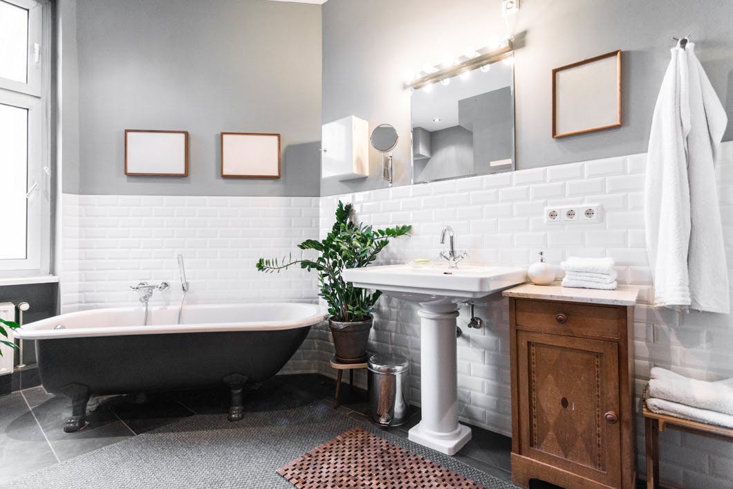Clean interior of modern apartment bathroom with white tiled walls, black free standing bathtub and tiled floor